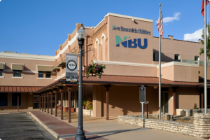A tan building with a sign reading "New Braunfels Utilities NBU," U.S. and Texas flags, and a streetlamp with a "Downtown" banner in front.