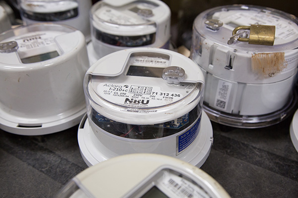 Several digital electric utility meters are grouped together on a flat surface, with one meter padlocked on top.