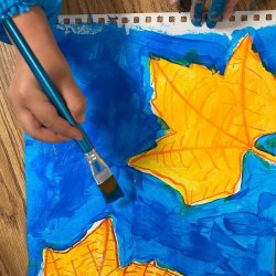 Child's hand painting water and a leaf with watercolors