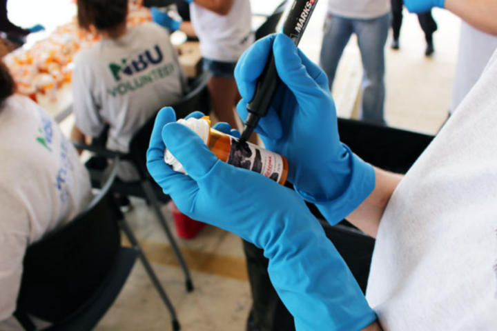 NBU Volunteer holds pill bottle in hand, scratching out personal information for safe disposal